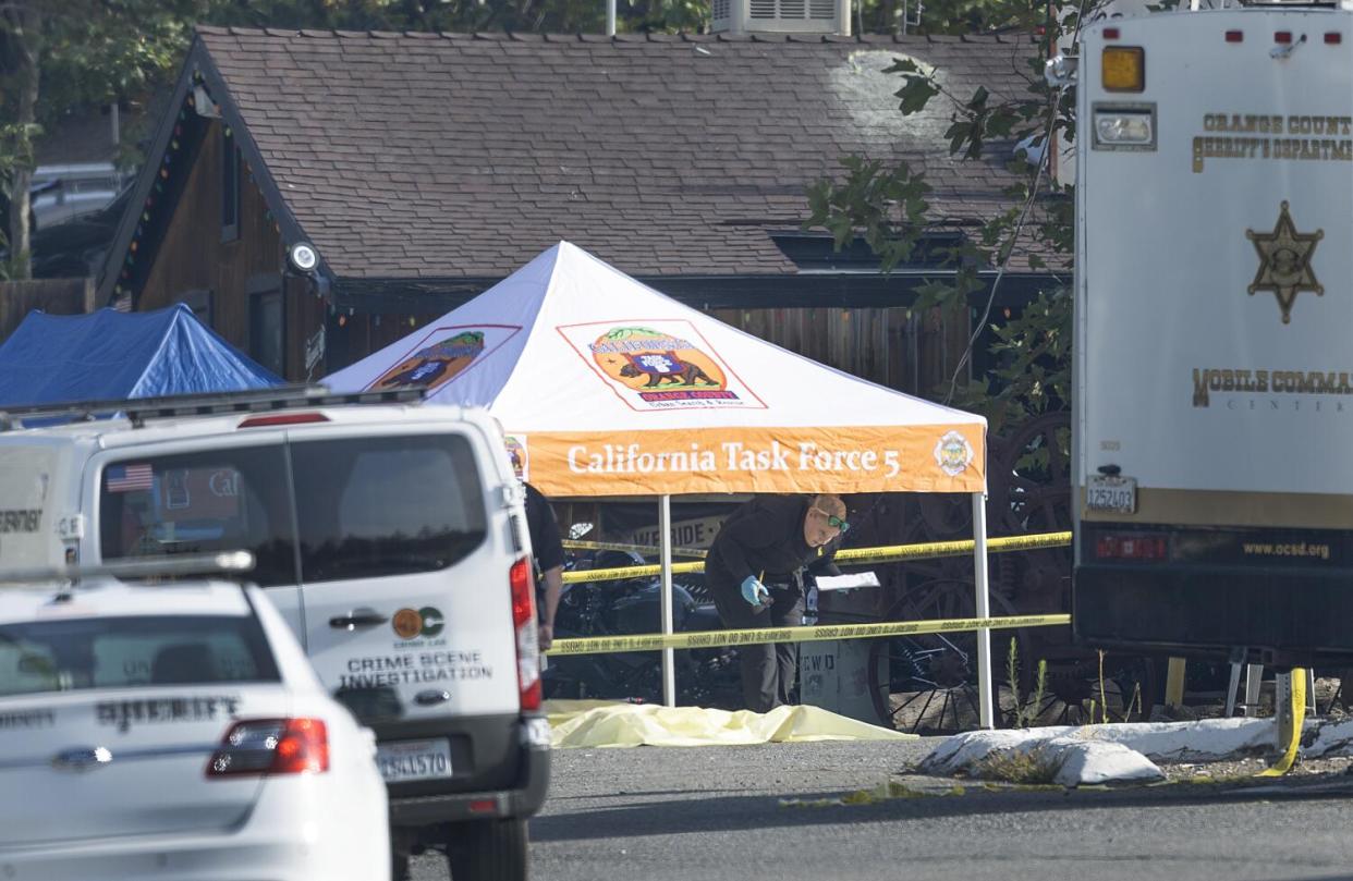 A tarp covers a body as Orange County crime scene investigators view the scene where a gunman killed three people