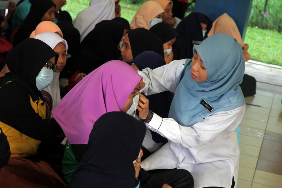 A teacher from SK Pasir Gudang 4 helps a student put on a face mask in Pasir Gudang, Johor June 30, 2019. — Bernama pic