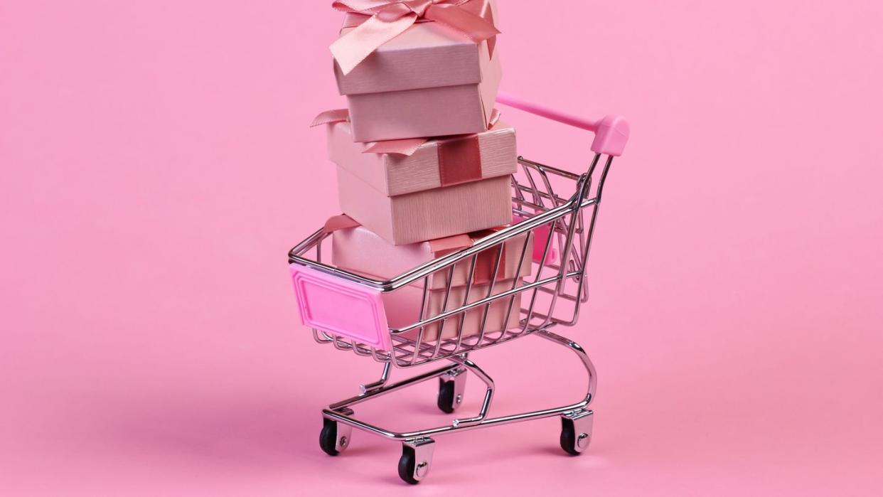 small grocery cart with pink presents inside on a pastel pink background