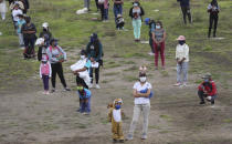 Niños y sus padres están en un campo manteniendo su distancia y usando mascarillas para protegerse de nuevo coronavirus mientras esperan regalos del día del niño en Yaruqui, cerca de Quito, en Ecuador, el lunes 1 de junio de 2020. (AP Foto/Dolores Ochoa)