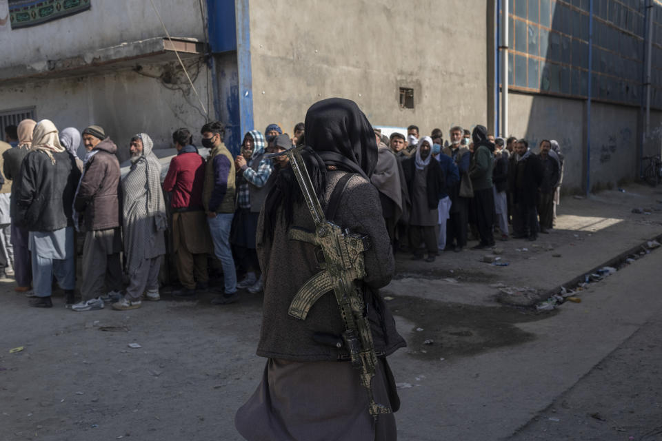 A Taliban fighter secures the area as people queue to receive cash at a money distribution site organized by the World Food Program (WFP) in Kabul, Afghanistan, Wednesday, Nov. 17, 2021. (AP Photo/Petros Giannakouris)