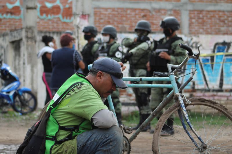 A man sits as soldiers keep watch outside a drug rehabilitation facility where assailants killed several people, according to Guanajuato state police, in Irapuato