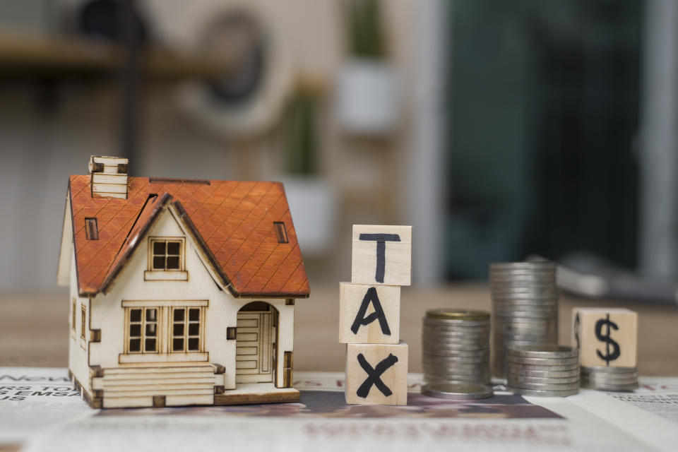 Tax text written on wooden block with stacked coins, illustrating a story on capital gains tax on property.