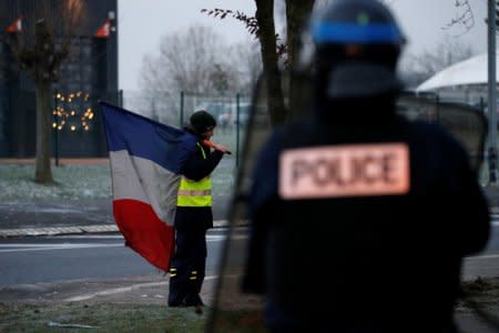 A protester wearing a yellow vest holds a French flag as the authorities dismantle their shelter at a traffic island near the A2 Paris-Brussels motorway in Fontaine-Notre-Dame, France, December 14, 2018.  REUTERS/Pascal Rossignol