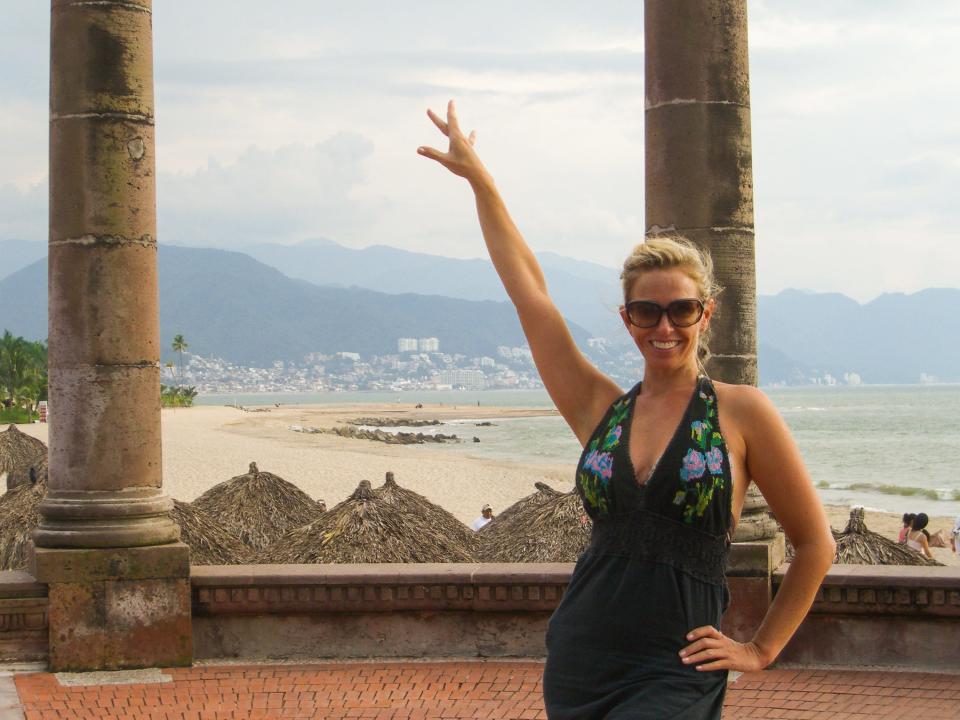 A woman poses in front of pillars and a beachy mountain scene