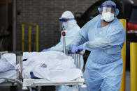 Medical workers wearing personal protective equipment wheel bodies to a refrigerated trailer serving as a makeshift morgue at Wyckoff Heights Medical Center, Monday, April 6, 2020, in the Brooklyn borough of New York. The new coronavirus causes mild or moderate symptoms for most people, but for some, especially older adults and people with existing health problems, it can cause more severe illness or death. (AP Photo/John Minchillo)