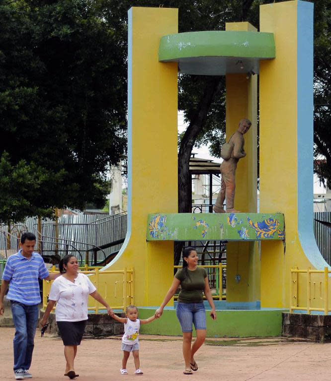 A family walks in front of a monument honouring Sifredo Chavez, the first migrant who traveled in 1967 from his home village to the US, in Intipuca