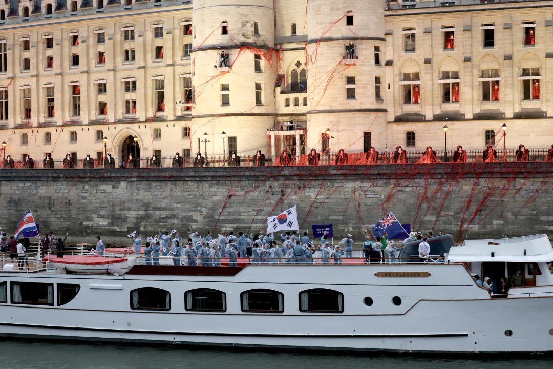 Members of Team Costa Rica, Team Republic of Korea and Team Cook Islands wave flags from a boat.