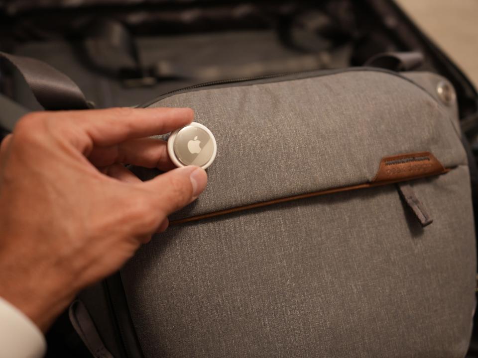 hand holding an airtag in front of a suitcase