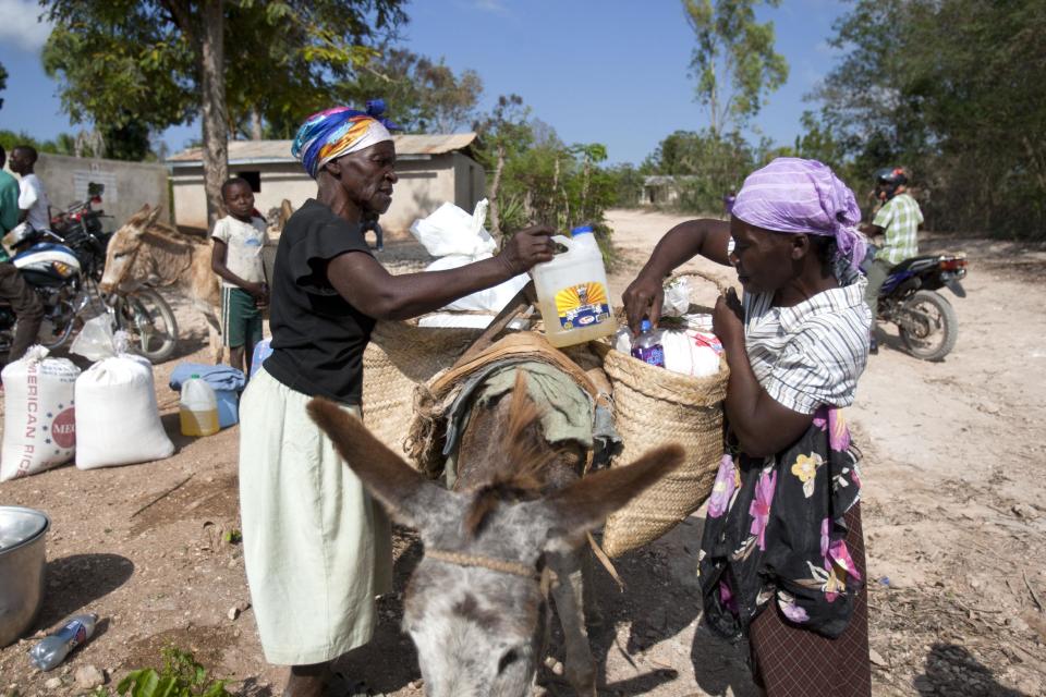 In this Monday, March 24, 2014 photo, two women pack cooking oil into donkey side sacks distributed by the U.N. World Food Program, WFP, at a local school in Bombardopolis, northwest Haiti. Drought is hitting this region, one of the hungriest, most desolate parts of the most impoverished nation in the hemisphere and it has alarmed international aid organizations such as the WFP, which sent workers this week to pass out bulgur wheat, cooking oil and salt.(AP Photo/Dieu Nalio Chery)