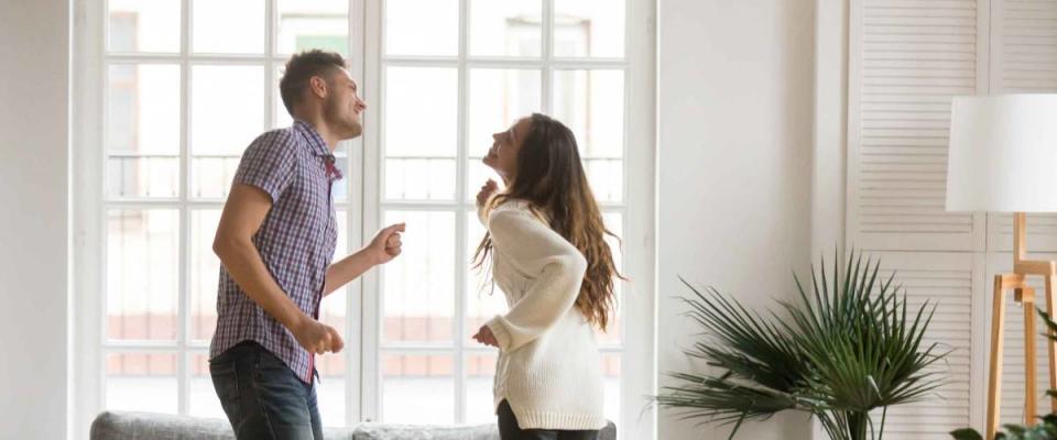 Young romantic carefree couple in love dancing spending time together at home, cheerful smiling man and woman having fun in cozy modern living room, happy husband and wife enjoying weekend