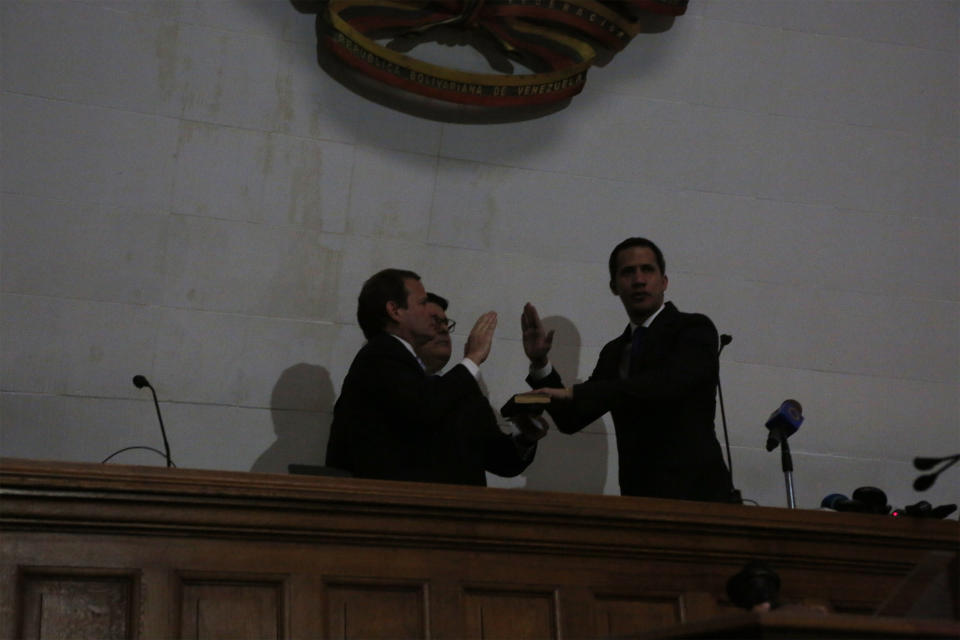 With the power out, opposition leader Juan Guaido, right, is sworn-in as the president of the National Assembly by lawmaker Juan Pablo Guanipa in Caracas, Venezuela, Tuesday, Jan. 7, 2020. Guaidó and opposition lawmakers pushed their way into Venezuela’s legislative building Tuesday following a standoff with security forces as the nation’s political divide deepens. (AP Photo/Andrea Hernandez Briceño)