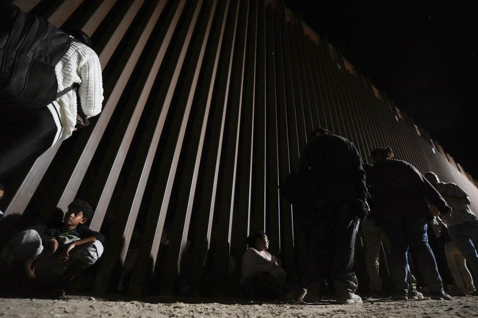 People line up against a border wall as they wait to apply for asylum after crossing the border from Mexico Tuesday, July 11, 2023, near Yuma, Arizona. Thousands of migrants from the north African country of Mauritania have arrived in the U.S. in recent months, following a new route taking them to Nicaragua and up through the southern border. (AP Photo/Gregory Bull)