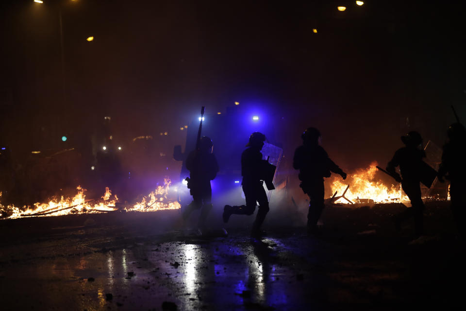 Police officers run past burning barricades on the fifth day of protests over the conviction of a dozen Catalan independence leaders in Barcelona, Spain, Friday, Oct. 18, 2019. Tens of thousands of flag-waving demonstrators demanding Catalonia's independence and the release from prison of their separatist leaders had earlier flooded downtown Barcelona. (AP Photo/Manu Fernandez)