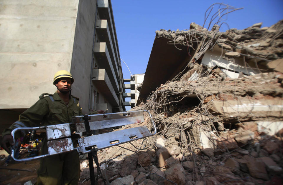 A rescue worker stands with a stretcher near the debris of a building that collapsed in Canacona, about 70 kilometers (44 miles) from Goa state capital Panaji, India, Sunday, Jan. 5, 2014. The five-story building under construction in the southern Indian state of Goa collapsed on Saturday, killing at least a dozen people and leaving dozens more feared trapped under the rubble, police said. (AP Photo/Rafiq Maqbool)