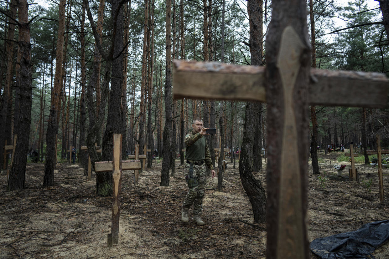 Oleg Kotenko, the Commissioner for Issues of Missing Persons under Special Circumstances uses his smartphone to film the unidentified graves of civilians and Ukrainian soldiers in the recently retaken area of Izium, Ukraine, Thursday, Sept. 15, 2022, who had been killed by Russian forces near the beginning of the war. A mass grave of Ukrainian soldiers and unknown buried civilians was found in the forest of recently recaptured city of Izium. (AP Photo/Evgeniy Maloletka)