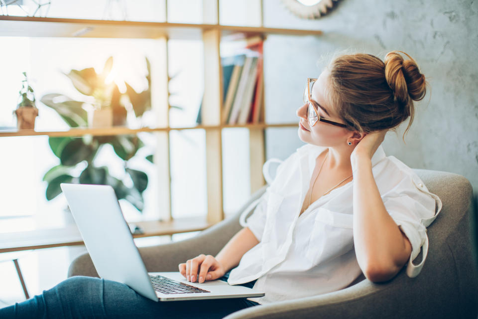 Young beautiful woman in her 20s wearing glasses working with a laptop while sitting in a chair in an alternative office.