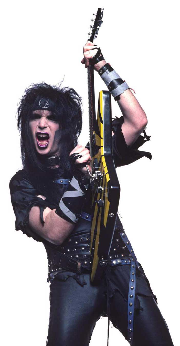 Mick Mars posing in a studio portrait with guitar held vertically