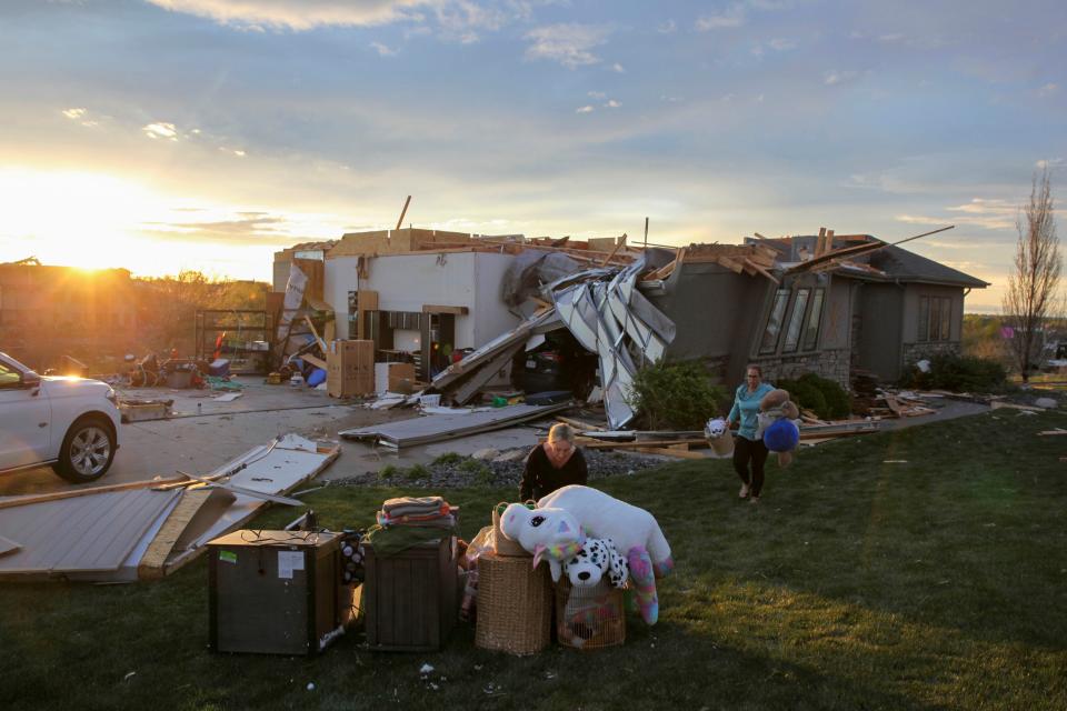 Two women help carry a friend's belongings out of their damaged home after a tornado passed through the area in Bennington, Neb., Friday, April 26, 2024. (AP Photo/Josh Funk)