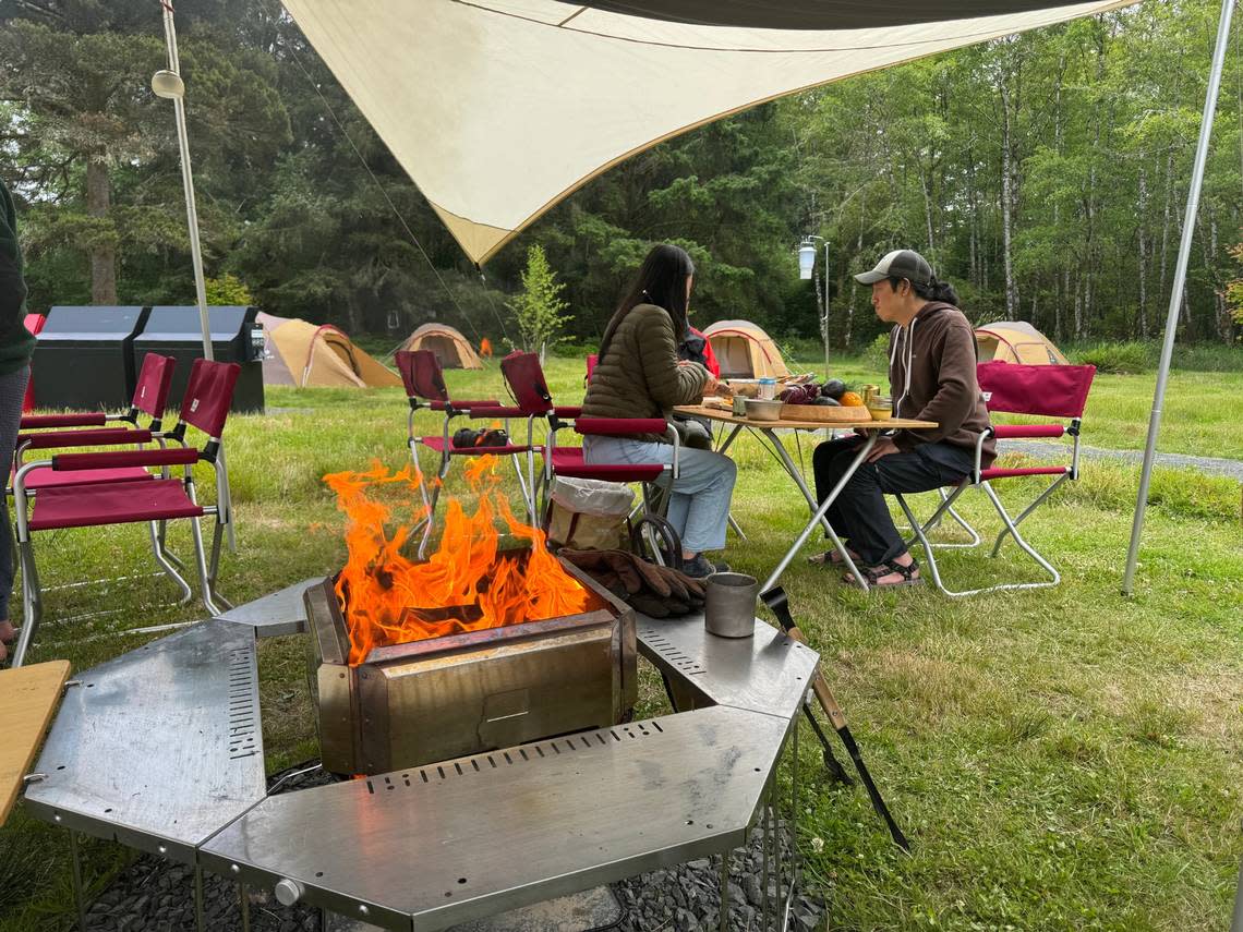 Campers relax near a flaming grill at Snow Peak’s Campfield Long Beach.