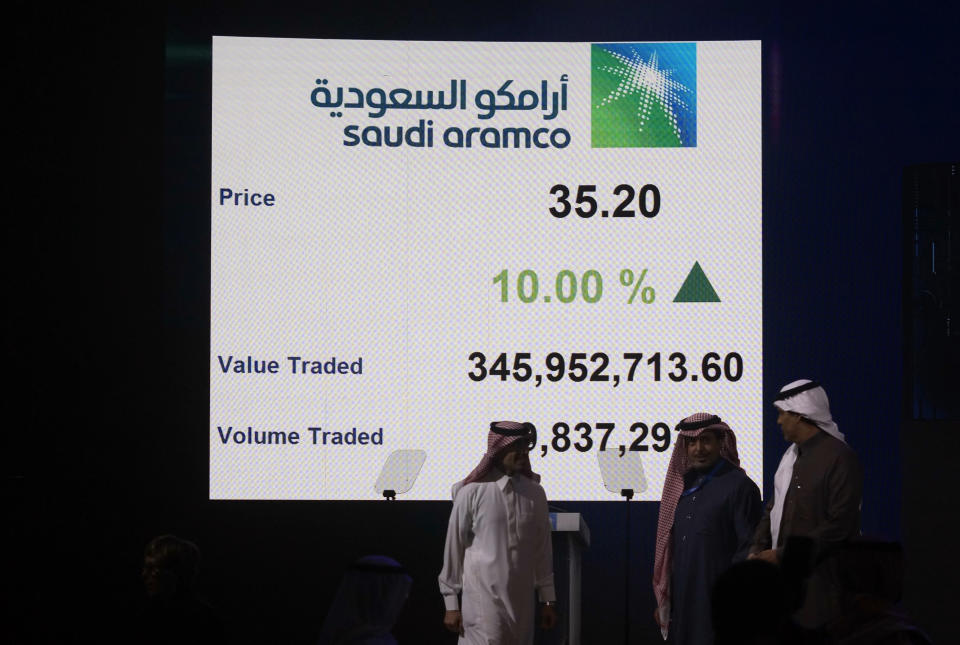 Saudi Arabia's state-owned oil company Armco and stock market officials walk under a screen displaying the value traded and the volume traded of Aramco's initial public offering (IPO) on the Riyadh's stock market, in Riyadh, Saudi Arabia, Wednesday, Dec. 11, 2019. (AP Photo/Amr Nabil)
