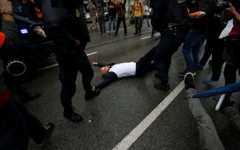 Spanish National Police drags away a man lying on the street as they try to prevent voters from reaching a voting site at a school assigned to be a polling station by the Catalan government in Barcelona - Credit: AP