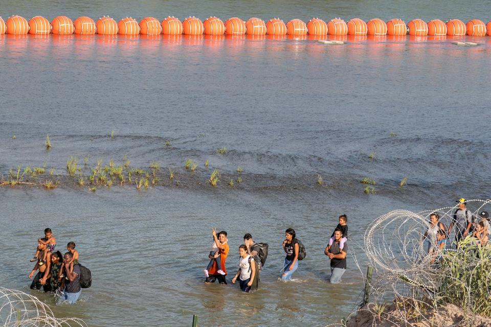 Migrants walk between a wire fence and a string of buoys in the Rio Grande on July 16, 2023. <a href="https://www.gettyimages.com/detail/news-photo/migrants-walk-between-concertina-wire-and-a-string-of-buoys-news-photo/1536221750?adppopup=true" rel="nofollow noopener" target="_blank" data-ylk="slk:Suzanne Cordeiro/AFP via Getty Images;elm:context_link;itc:0;sec:content-canvas" class="link ">Suzanne Cordeiro/AFP via Getty Images</a>