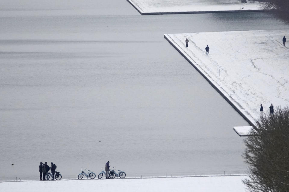 Tourists stroll by the canal in the gardens of the Chateau de Versailles Tuesday, Jan. 9, 2024 in Versailles, west of Paris, where temperatures fell under zero degree Celsius (32 degrees Fahrenheit). (AP Photo/Christophe Ena)