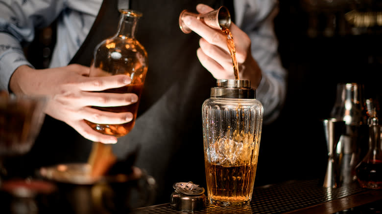 Bartender pours brown liquor into cocktail shaker