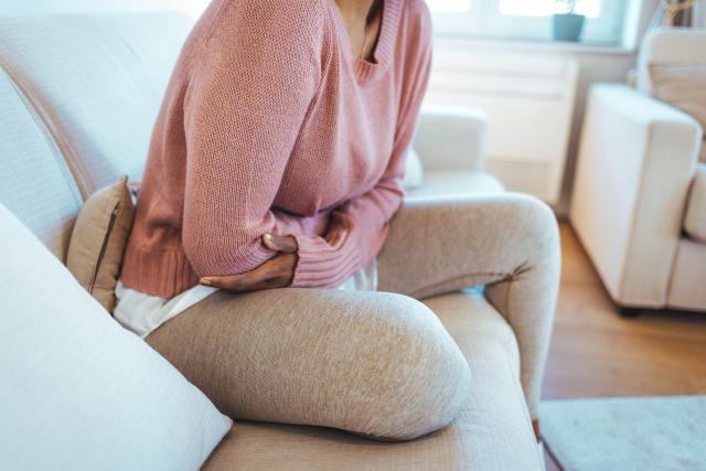 Woman on sofa hunched over with period pain. (Getty Images)