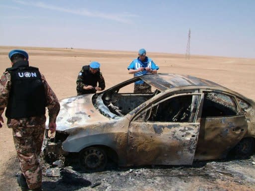 A handout picture released by the official Syrian Arab News Agency (SANA) on May 14, shows UN observers inspecting a burnt car which was targeted in Deir Ezzor. A convoy of UN truce observers came under attack in a Syrian town on Tuesday during a funeral procession in which a monitoring group said regime forces "massacred" 20 people