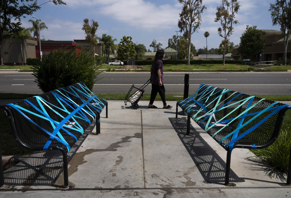 Una mujer camina frente a unas bancas inhabilitadas para implementar las medidas de distanciamiento social afuera de un restaurante en La Habra, California, el jueves 2 de julio de 2020. (AP Foto/Jae C. Hong)