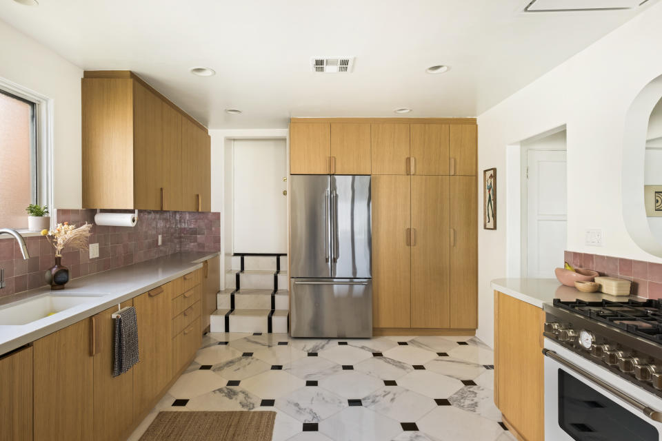 A kitchen with marble tiled flooring, wooden cabinetry, and a pink backsplash