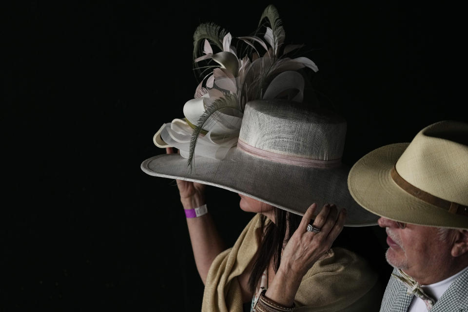 Una mujer se ajusta su sombrero antes de la carrera de caballos número 148 de las carreras del Derby de Kentucky, el 7 de mayo de 2022, en Churchill Downs en Louisville, Kentucky. (AP Foto/Charlie Riedel)