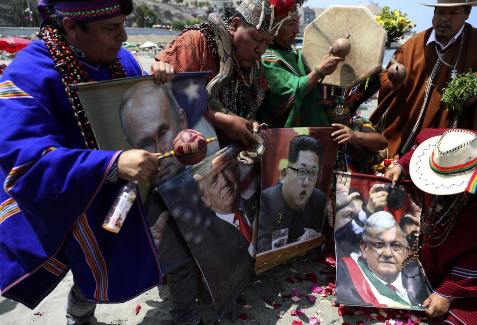 Shamans holding posters that show Russian President Vladimir Putin, left, U.S. President Donald Trump, North Korean leader Kim Jong and Mexico's President Andres Manuel Lopez Obrador, perform their annual pre-New Year ceremony on Agua Dulce beach in Lima, Peru, Thursday, Dec. 27, 2018. Peruvian shamans came together for their yearly ritual, making predictions for what the New Year has in store. The ritual, which incorporates music and chanting, revealed that the year 2019 will bring about peaceful relations between warring countries. (AP Photo/Martin Mejia)