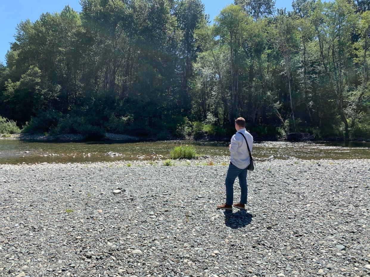 Aaron Stone, chair of the Cowichan Valley Regional District and co-chair of the Cowichan Watershed Board, stands on the banks of the Cowichan River in July 2023. He is one of many who have been calling for provincial funding for a new weir, which would help keep water flowing in the summer. (Kathryn Marlow/CBC - image credit)