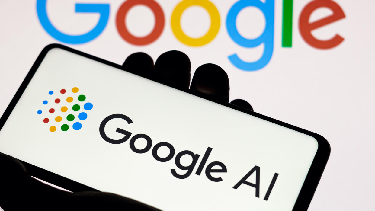  A Google AI logo is on a phone held in a hand, in front of a Google Logo 