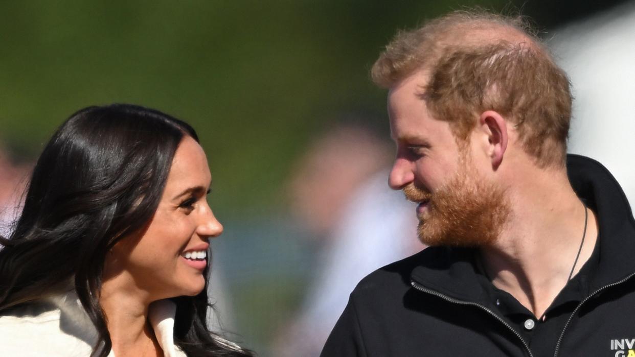 Meghan Markle and Prince Harry walking hand-in-hand on an athletics track