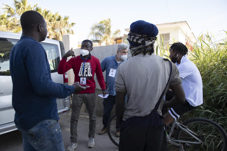 In this photo taken on Monday, April 27, 2020, father Daniele Moschetti, right, and Appiah Kwasi from Ghana, a cultural mediator, explain migrants how to apply for food, as they walk in Castel Volturno, near Naples, Southern Italy. Father Daniele Moschetti spent a decade doing missionary work in the slums of Nairobi and now he finds his work to be similar in his own country. They are known as “the invisibles,” the undocumented African migrants who, even before the coronavirus outbreak plunged Italy into crisis, barely scraped by as day laborers, prostitutes and seasonal farm hands. Locked down for two months in their overcrowded apartments, their hand-to-mouth existence has grown even more precarious with no work, no food and no hope. (AP Photo/Alessandra Tarantino)