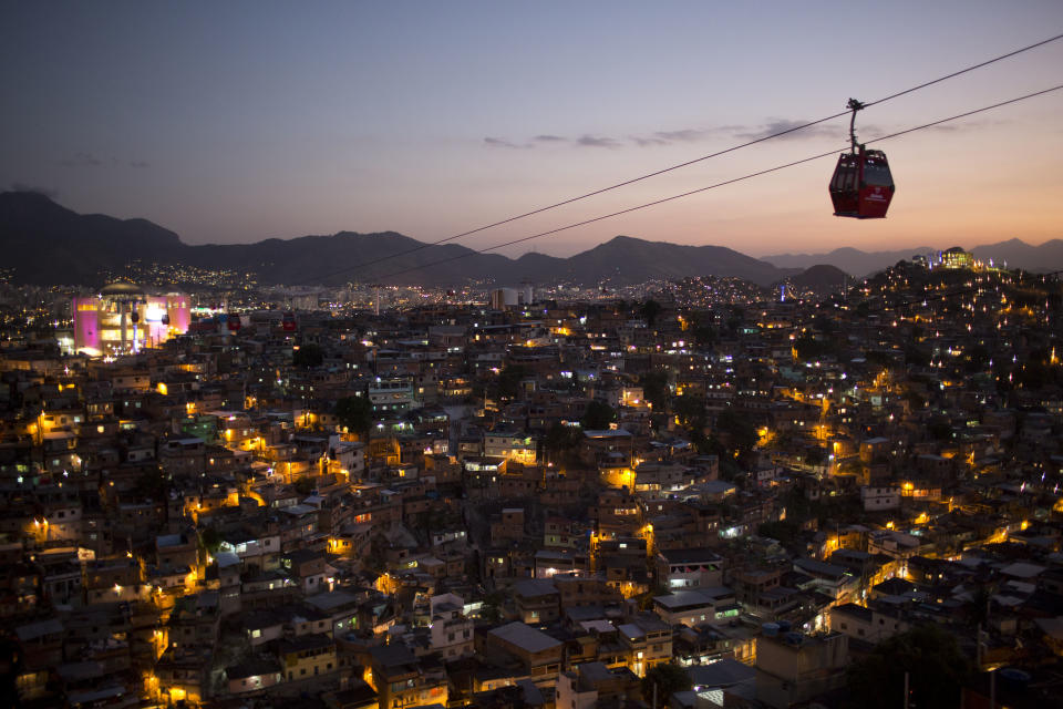 In this May 10, 2013 photo, homes are lit at night as cable-cars move commuters over the Complexo do Alemao complex of shantytowns in Rio de Janeiro, Brazil. The cable-car system linking six of its hilltops over a 3.5-kilometer (2.3-mile) route has become a popular tourist attraction. (AP Photo/Felipe Dana)