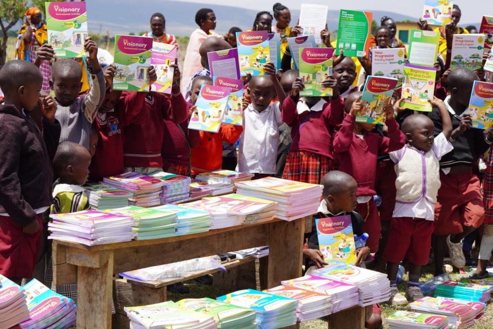 Maasai children holding up the textbooks funded through the Olalashe Foundation. Since the organization's inception, the Olalashe Foundation has helped bring 700 textbooks to Maasai schools.