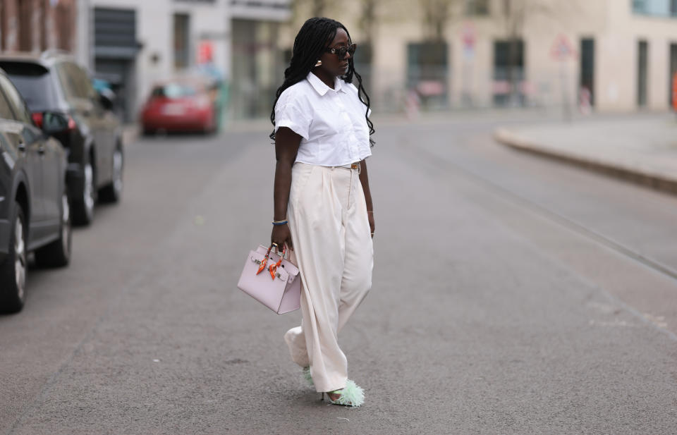 ASML ASOS - Lois Opoku wears beige suit pants by Julian Deinoff x Rossi, yellow gold belt in kelly white leather by Hermes, white blouse by ZARA, and Birkin 25 bag in beige and rose by Hermes with orange details , golden statement earrings from ASOS, and feather light green heels from ZARA in April.  January 2024, Berlin, Germany.  (Photo by Jeremy Mohler/Getty Images)