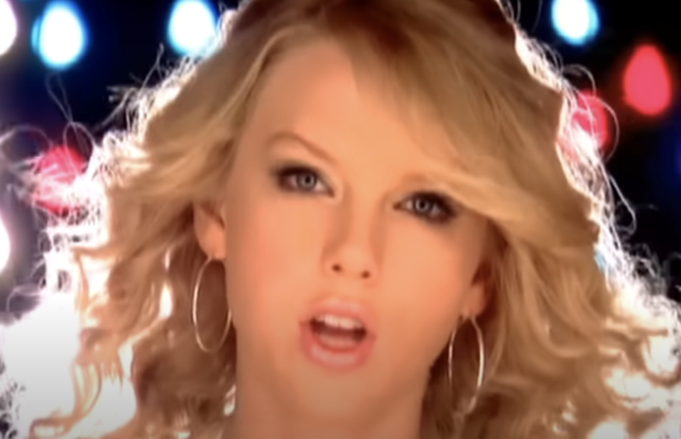 Close-up of Taylor Swift singing with bright stage lights in the background