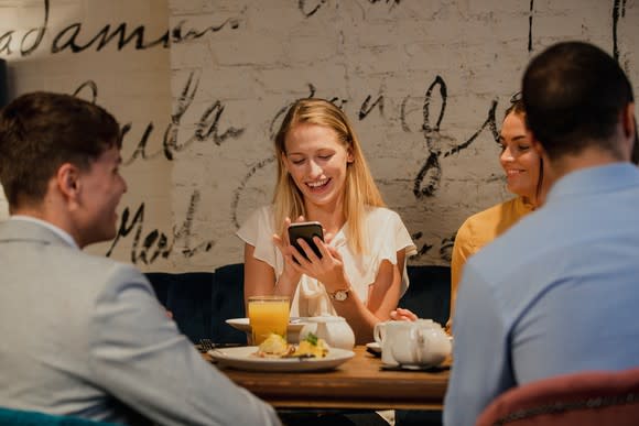 Friends dining in restaurant, woman holding mobile phone and smiling