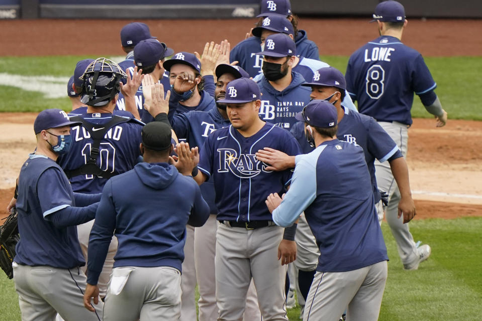 Tampa Bay Rays players congratulate designated hitter Yoshi Tsutsugo, center, who drove in the go-ahead run during the seventh inning of a baseball game against the New York Yankees, Sunday, April 18, 2021, at Yankee Stadium in New York. (AP Photo/Kathy Willens)
