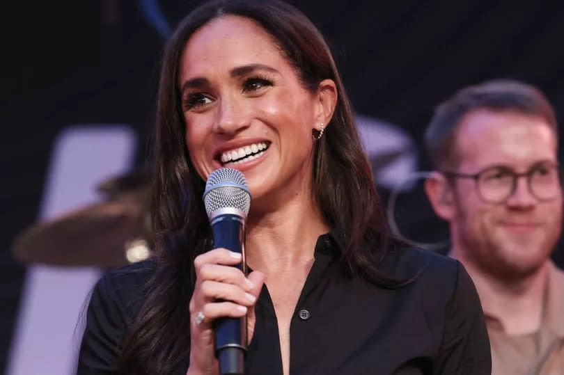 Meghan Markle speaking into a mic on stage wearing a black dress