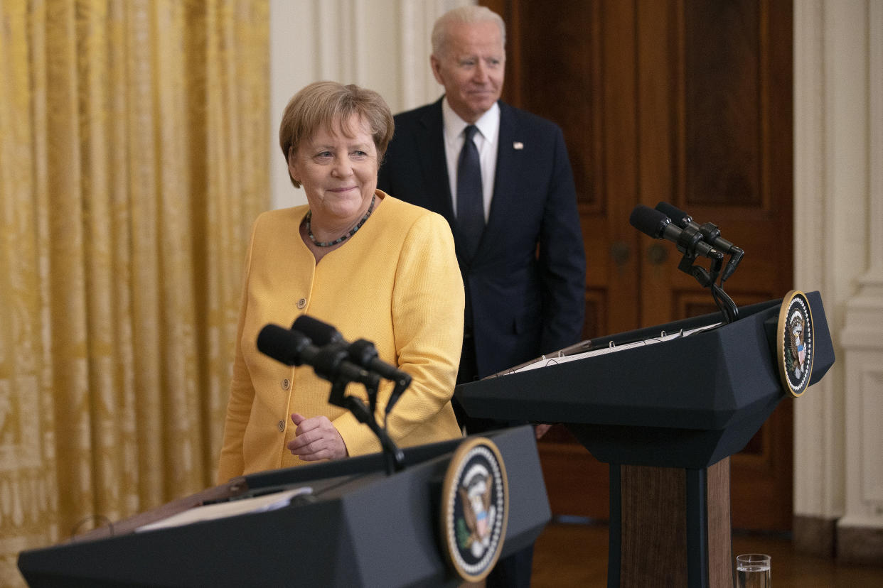 German Chancellor Angela Merkel and President Biden walk toward podiums bearing the presidential seal.