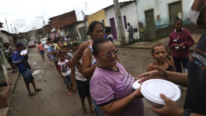 Warga yang terkena banjir mengantre untuk makanan yang disumbangkan di Itapetinga, negara bagian Bahia, Brasil, Selasa (28/12/2021). Banjir menyebabkan ribuan orang terpaksa mengungsi dari rumah mereka . (AP/Raphael Muller)