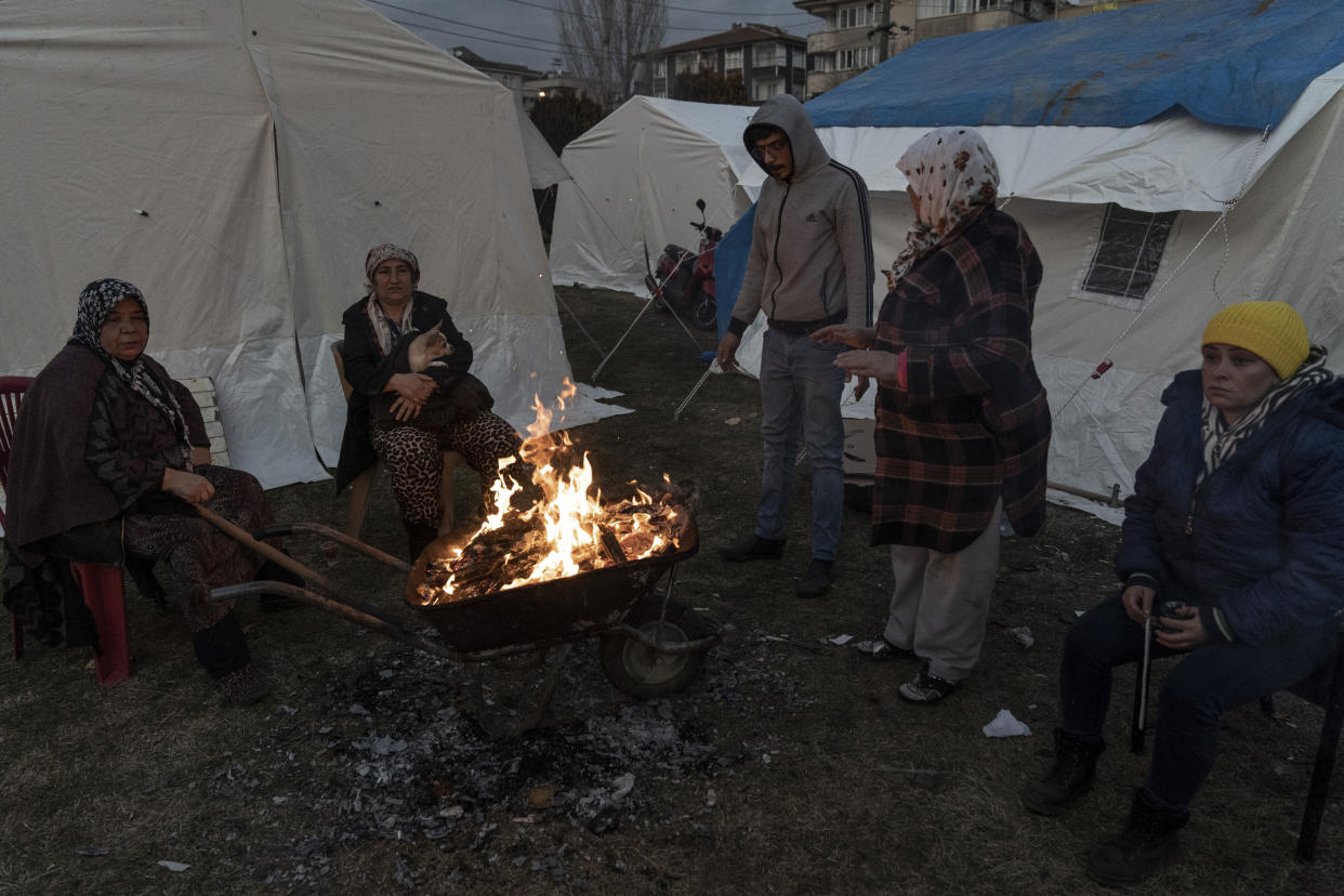 People keep warm next to a fire at a camp for survivors of the earthquake in Gaziantep, Turkey, Friday, Feb. 10, 2023. Emergency crews made a series of dramatic rescues in Turkey on Friday, pulling several people from the rubble four days after a catastrophic 7.8-magnitude earthquake killed thousands in Turkey and Syria. (AP Photo/Mustafa Karali)