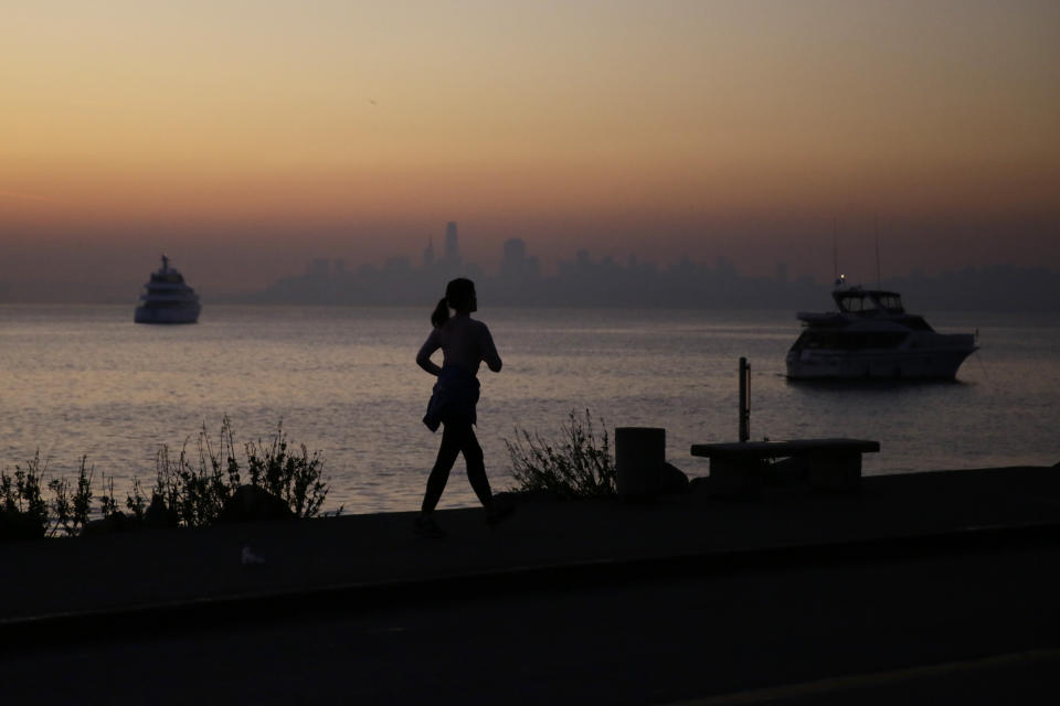 A woman walks along the waterfront Monday, Oct. 28, 2019, in Sausalito, Calif., as smoke from wildfires blankets the San Francisco skyline in the background. A wildfire that has been burning in Northern California's wine country since last week grew overnight as nearly 200,000 people remain under evacuation orders. (AP Photo/Eric Risberg)